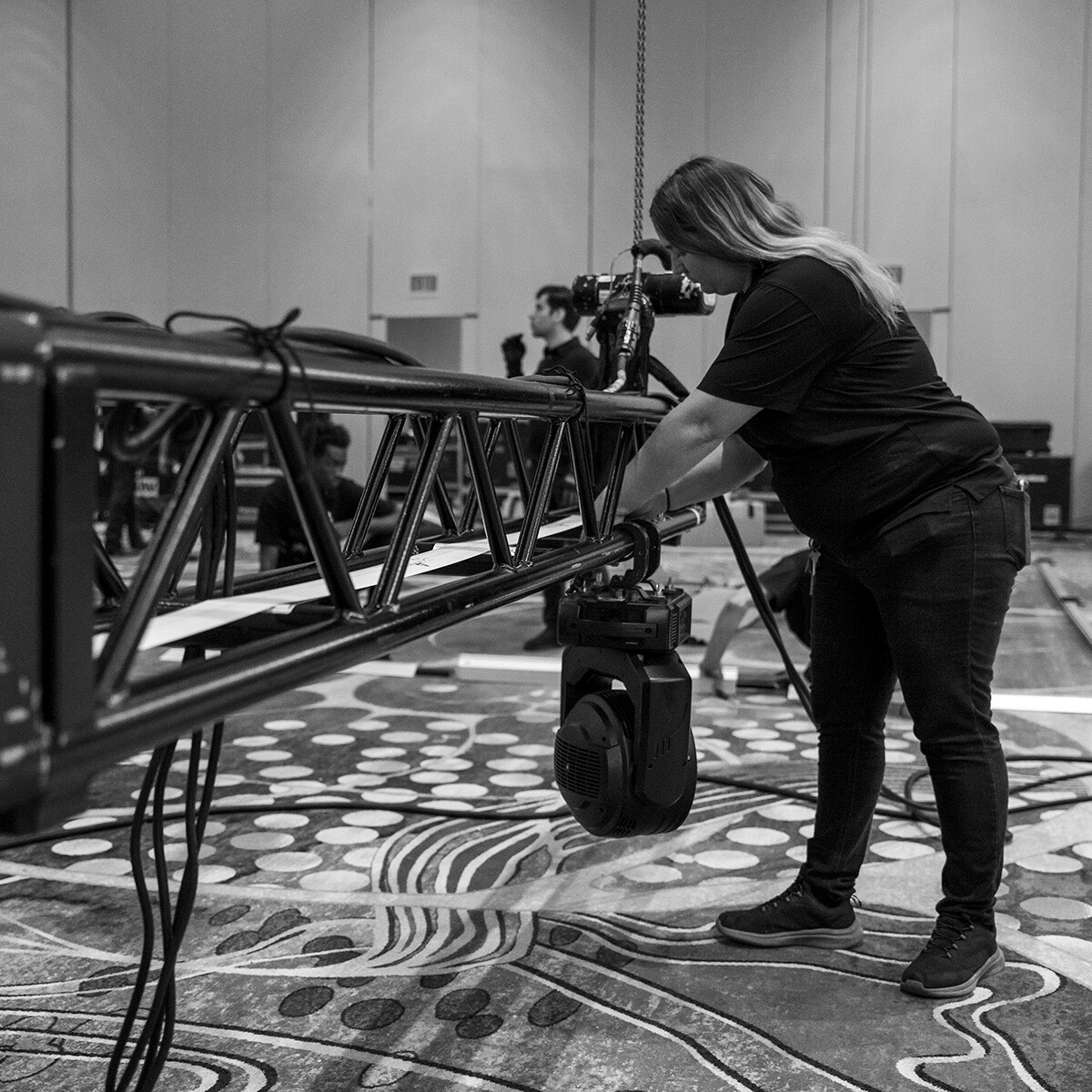 Woman securing a large truss for stage lighting setup.